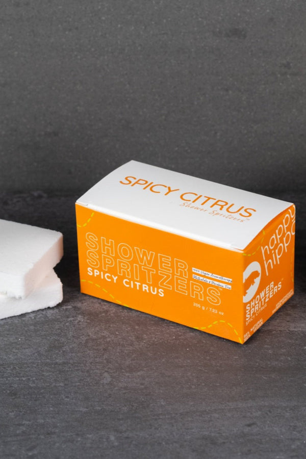 Spicy Citrus Shower Spritzer packaging and sponge on a dark surface.