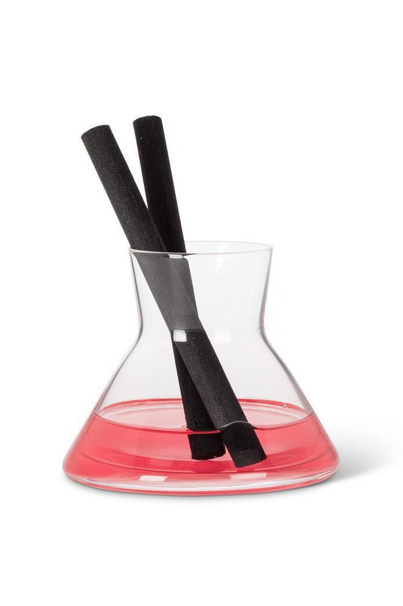 Clear glass beaker with pink bottom with clear oil and black diffuser rods on a white background