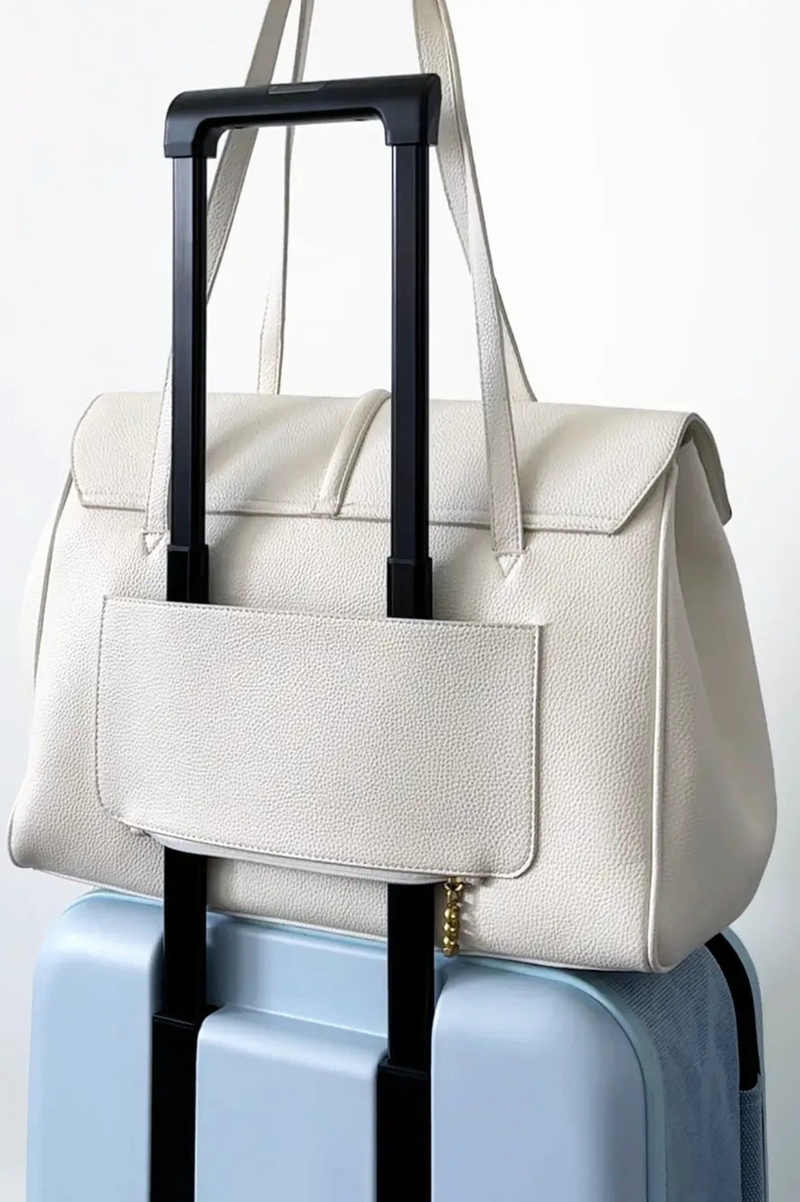 White handbag with black handle on a light blue suitcase against a white background