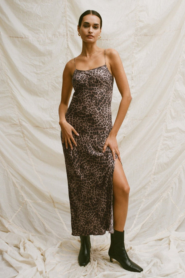 Woman wearing a leopard print dress with a slit on a textured white background