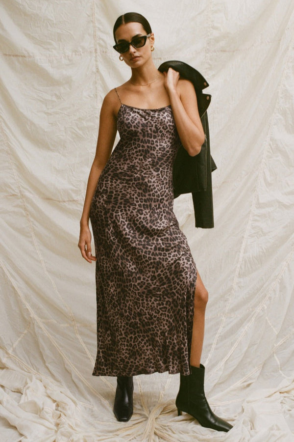 Woman wearing a leopard print dress with a black jacket over her shoulder against a white background