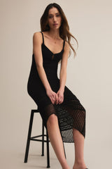 Woman wearing a black slip dress sitting on a stool against a beige background