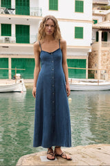 Woman in a blue dress standing by a waterfront with buildings in the background