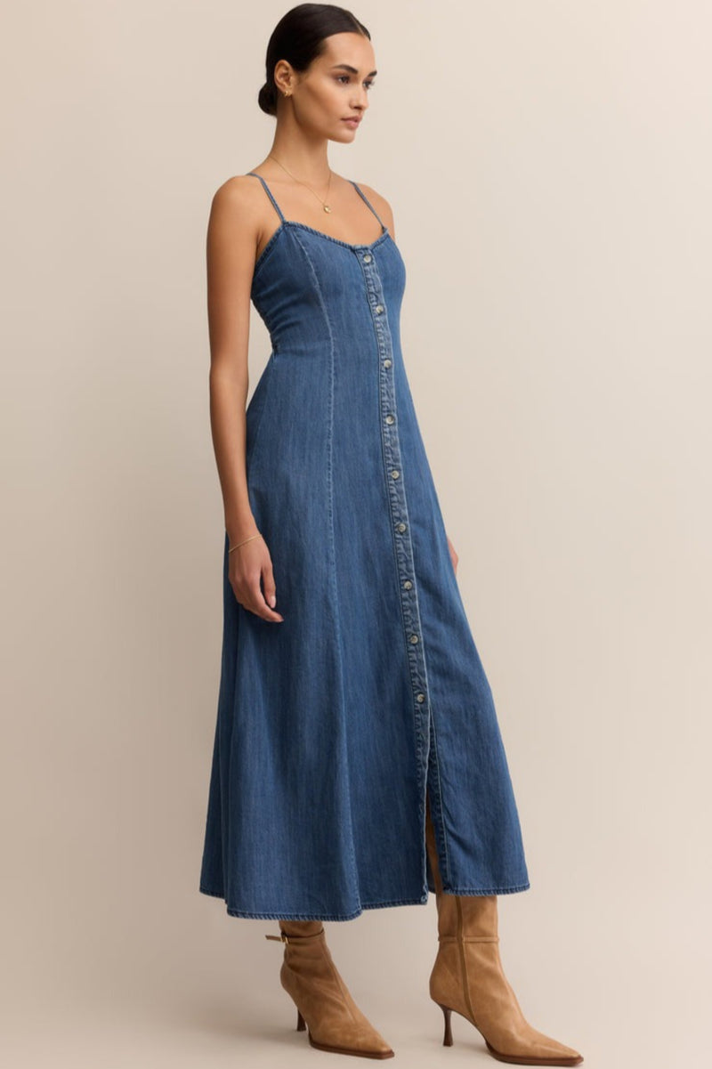 Woman wearing a blue denim dress with brown boots on a beige background