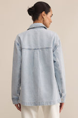 Woman wearing a light blue denim jacket against a beige background
