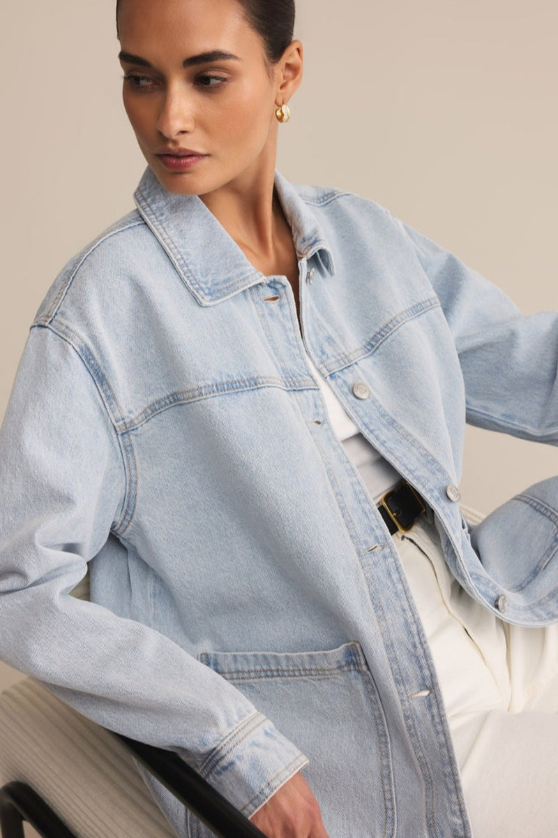 Woman wearing a light blue denim jacket against a neutral background