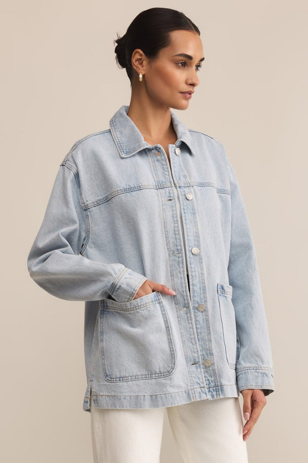Woman wearing a light blue denim jacket against a beige background