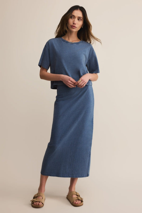 Woman wearing a blue top and skirt standing against a beige background