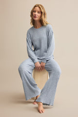 Woman wearing a blue ribbed pajama set sitting on a beige surface.
