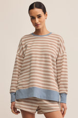 Woman wearing a striped pajama set with a beige and blue color scheme on a plain background