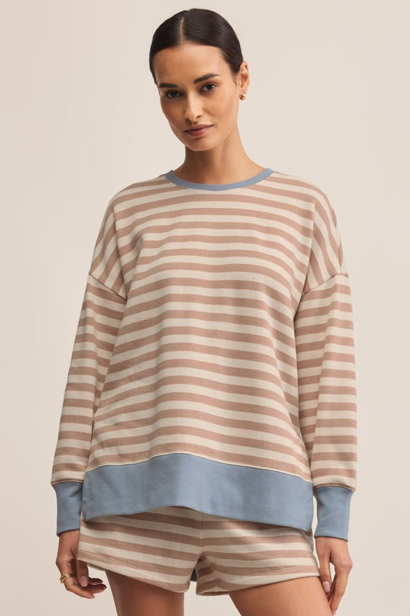 Woman wearing a striped pajama set with a beige and blue color scheme on a plain background