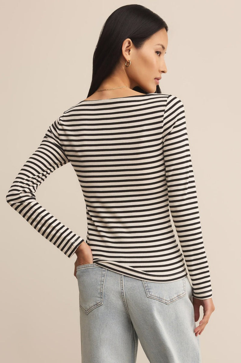 Woman wearing a black and white striped long-sleeve top with light blue jeans on a beige background