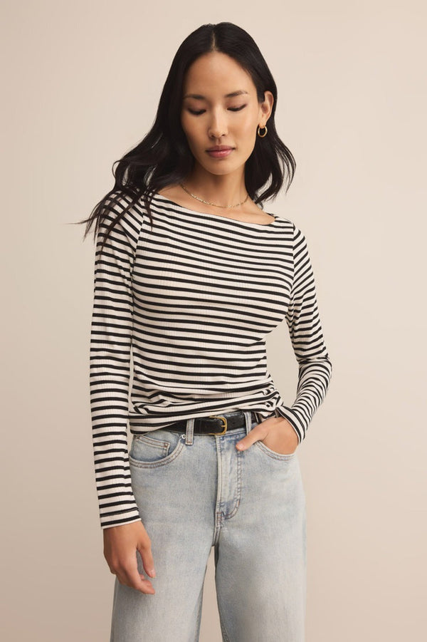 Woman wearing a black and white striped long-sleeve top and light blue jeans against a beige background