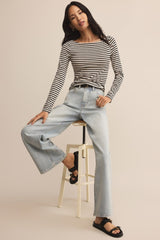 Woman wearing a striped shirt and jeans sitting on a stool against a beige background