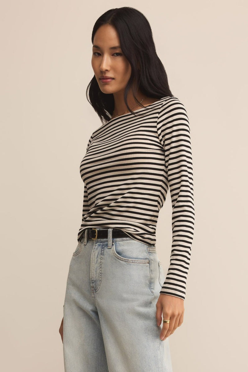 Woman wearing a black and white striped long-sleeve top and light blue jeans on a beige background