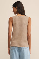 Woman wearing a beige sleeveless top and light blue jeans on a beige background