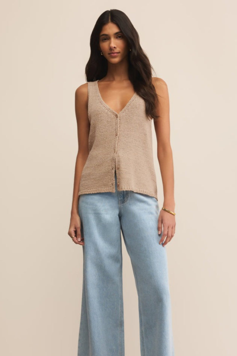 Woman wearing a beige sleeveless top and light blue jeans on a beige background