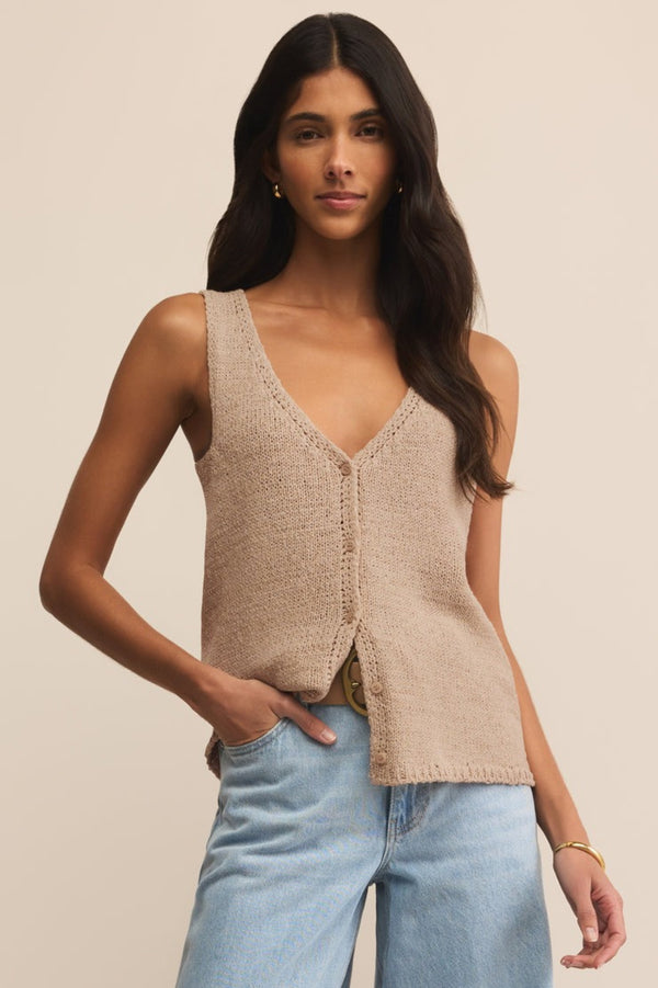 Woman wearing a beige knitted vest and light blue jeans against a neutral background