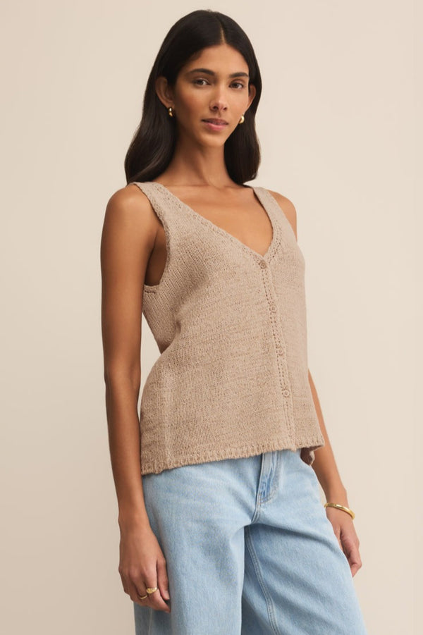 Woman wearing a beige knitted tank top and light blue jeans against a beige background