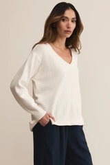Woman wearing a white sweater and dark pants against a beige background