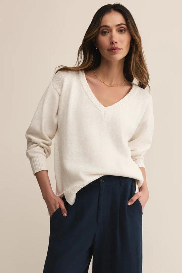 Woman wearing a white sweater and navy pants against a beige background