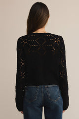 Person wearing a black knitted cardigan with a geometric pattern on a beige background