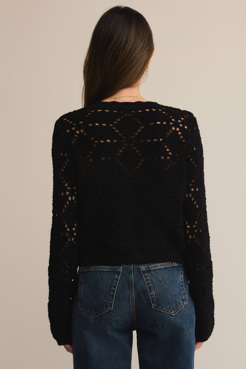 Person wearing a black knitted cardigan with a geometric pattern on a beige background