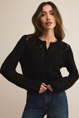 Woman wearing a black knitted cardigan and blue jeans against a beige background