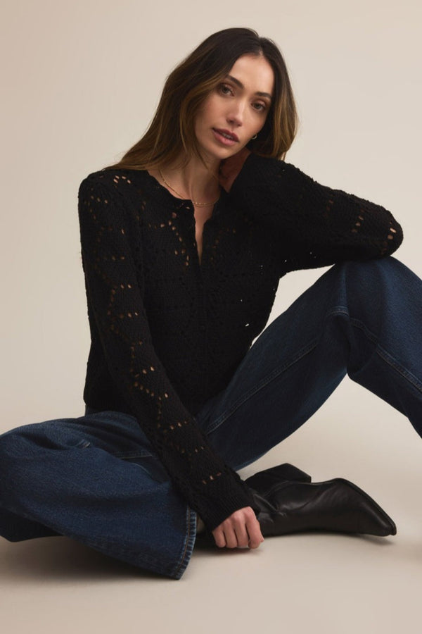 Woman wearing a black sweater and blue jeans sitting on the floor against a plain background
