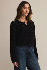 Woman wearing a black sweater and blue jeans against a beige background