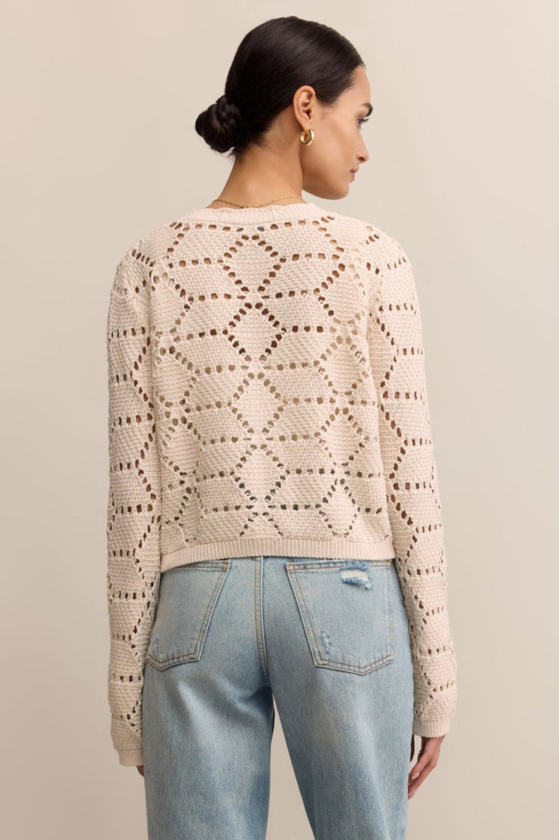 Woman wearing a beige patterned sweater and light blue jeans against a beige background