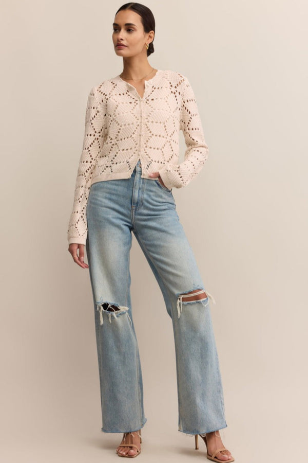 Woman wearing a light pink lace top and blue jeans on a beige background