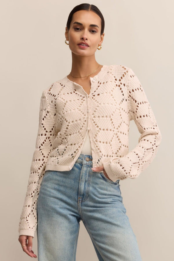 Woman wearing a light pink lace cardigan and blue jeans on a beige background