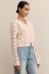 Woman wearing a light pink crochet sweater and light blue jeans against a neutral background