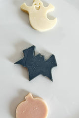 Three Halloween-themed cookies shaped like a ghost, bat, and pumpkin on a white plate.
