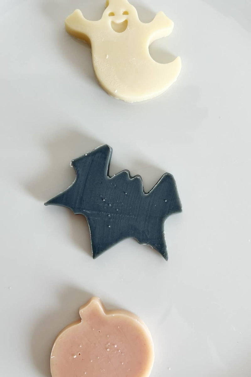 Three Halloween-themed cookies shaped like a ghost, bat, and pumpkin on a white plate.
