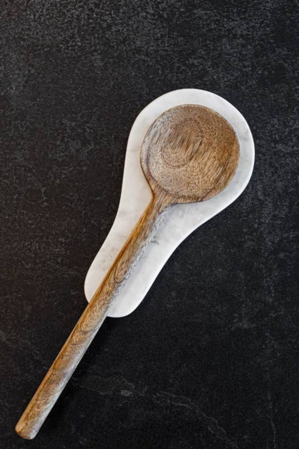 Wooden spoon on a marble spoon rest on a dark textured background