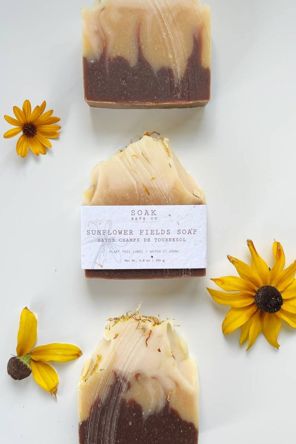 Three bars of soap with sunflower fields branding on a white background with sunflowers.