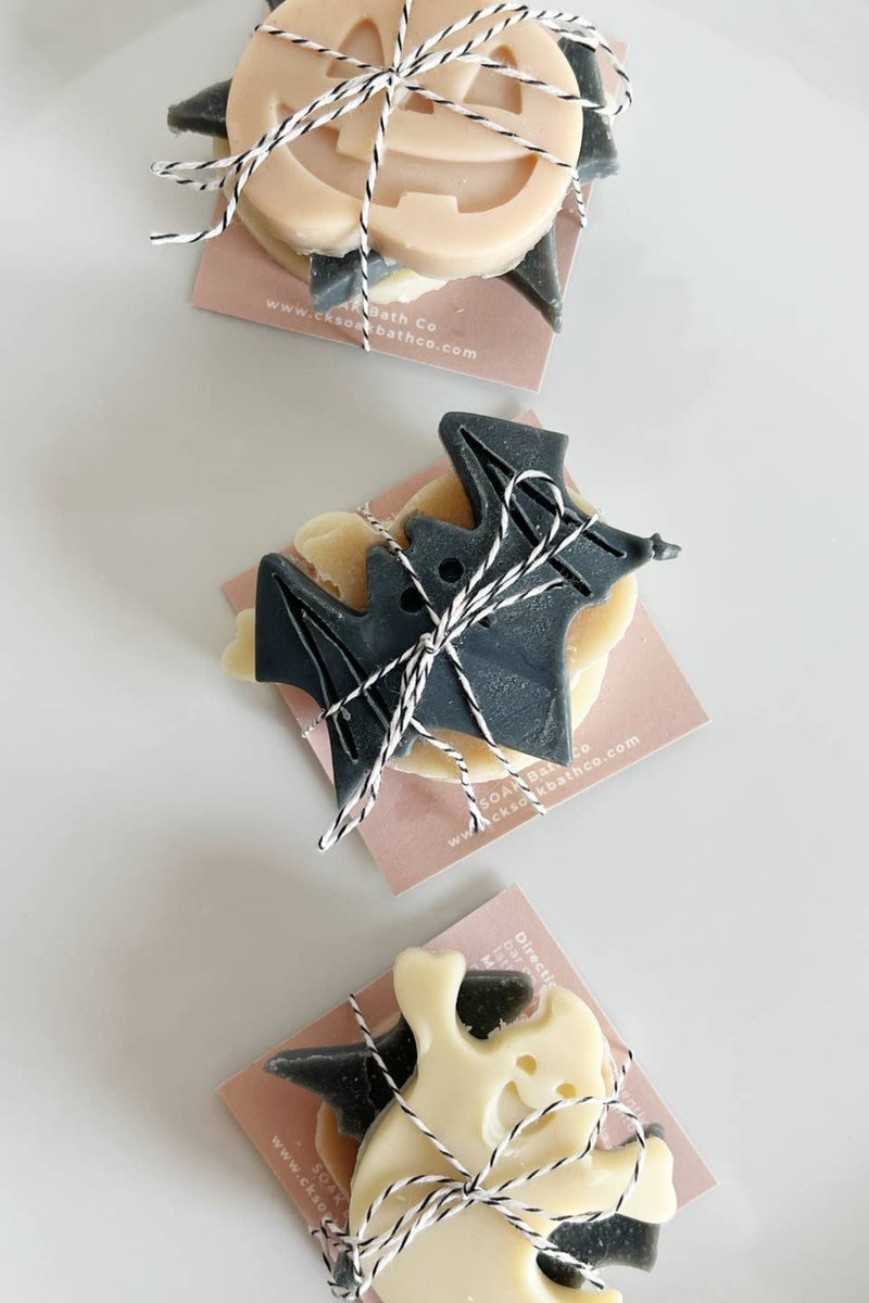 Three Halloween-themed soap bars on pink cards with string, on a white plate.