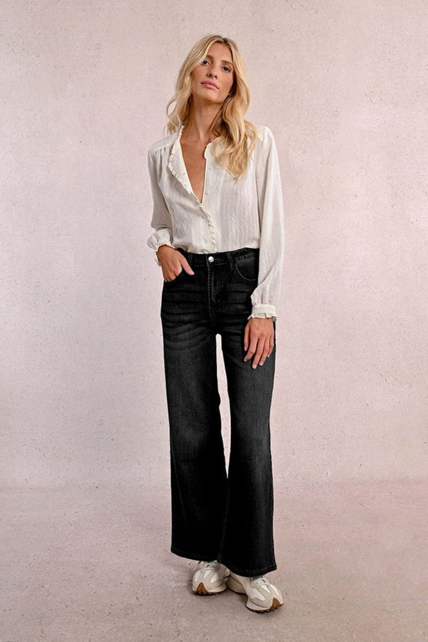 Woman wearing a white blouse and black jeans against a plain background