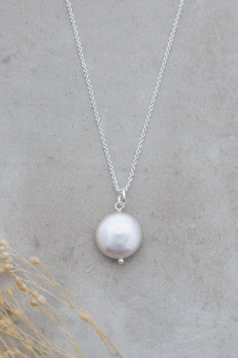 Pearl necklace on a chain against a gray background with dried plants.