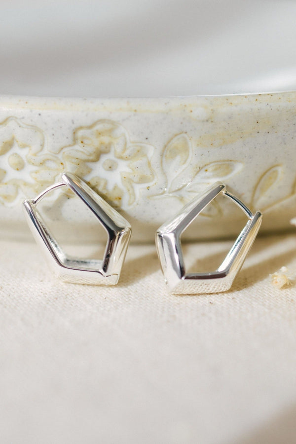 Silver geometric earrings on a textured beige surface