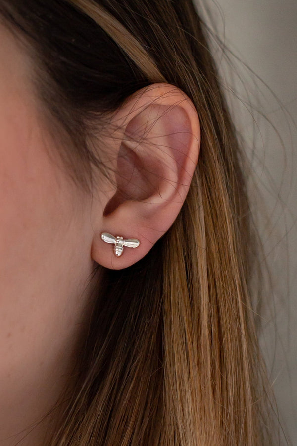 Close-up of an ear wearing a small silver earring with a neutral background
