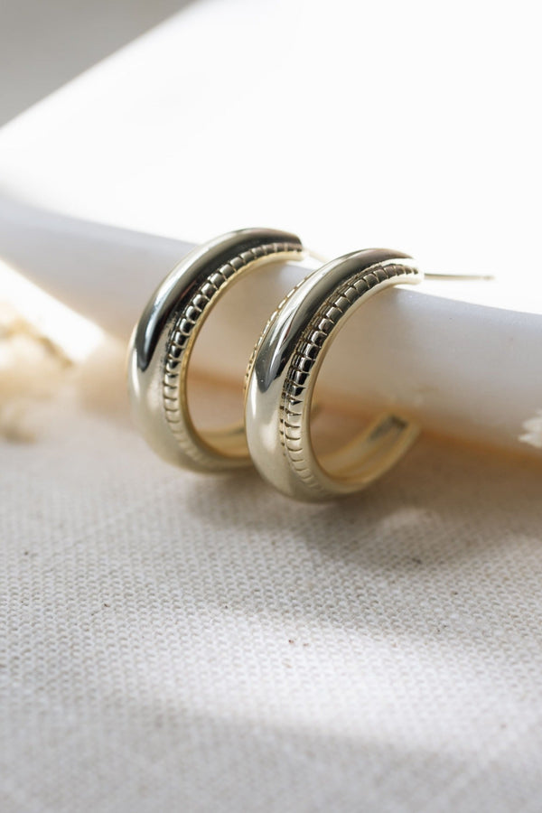 Gold hoop earrings on a white candle with a soft background