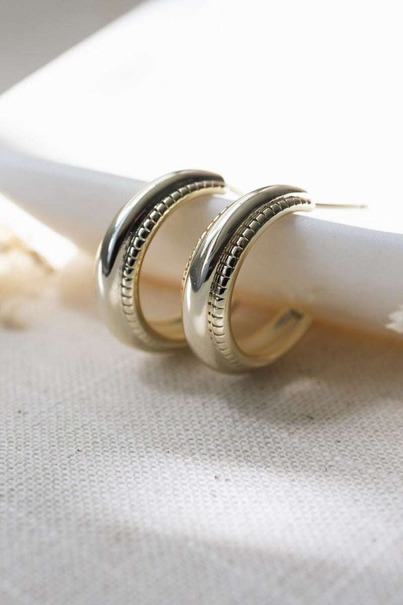 Gold hoop earrings on a white candle with a soft background