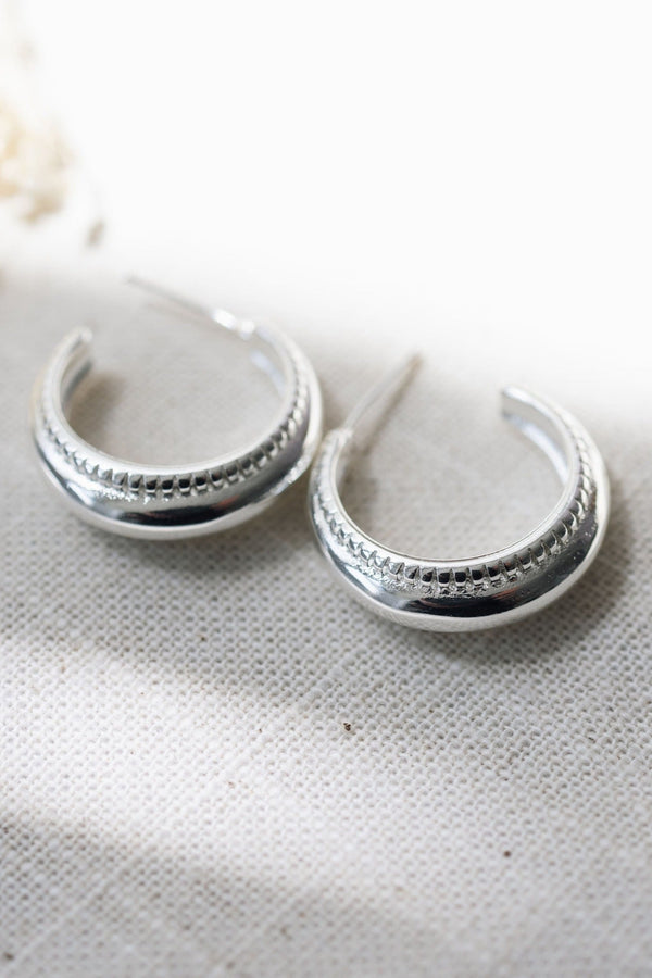 Silver hoop earrings on a textured white surface