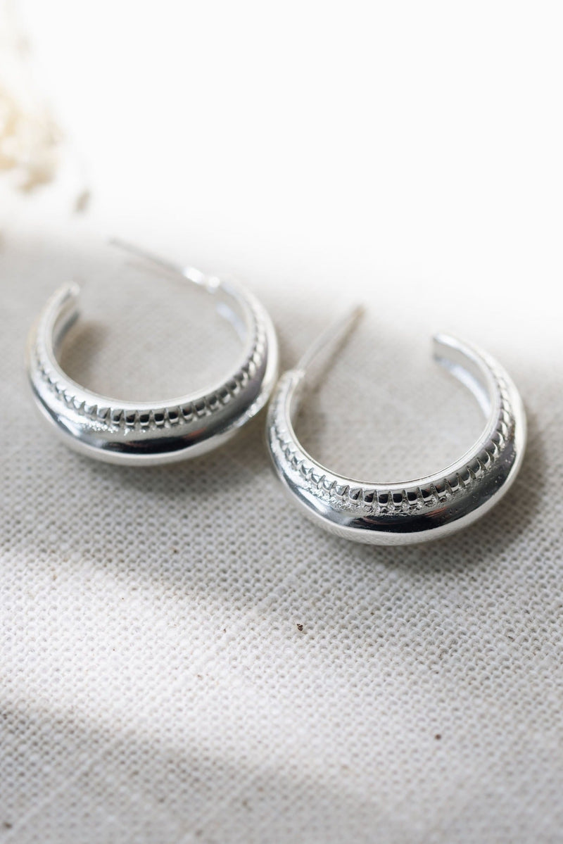 Silver hoop earrings on a textured white surface