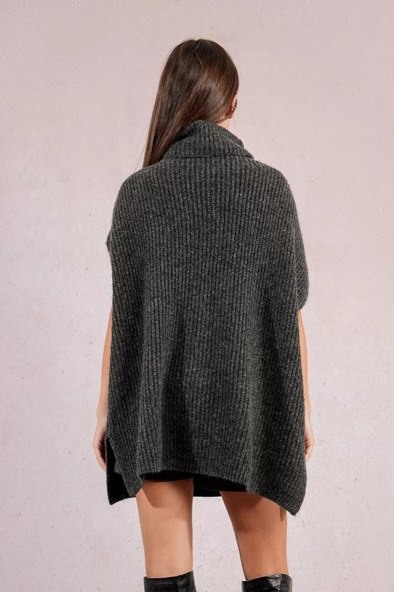 Person wearing a dark gray knitted poncho against a light background