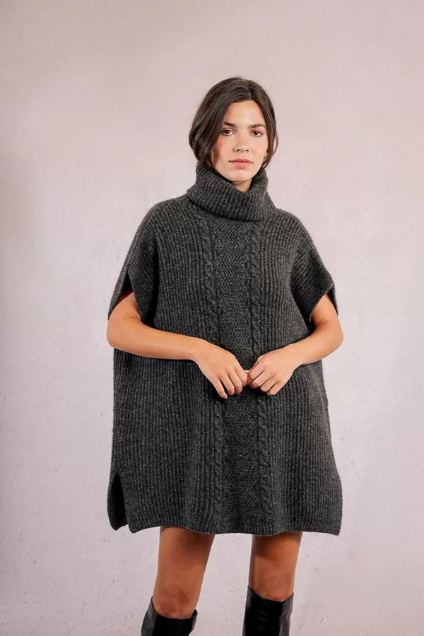 Woman wearing a dark gray knitted poncho against a plain background