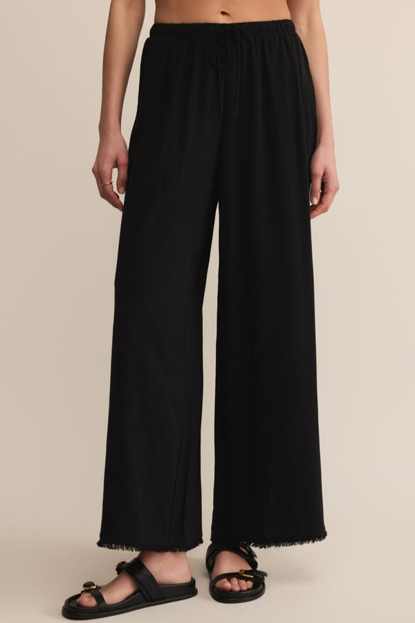 Person wearing black wide-leg pants on a beige background